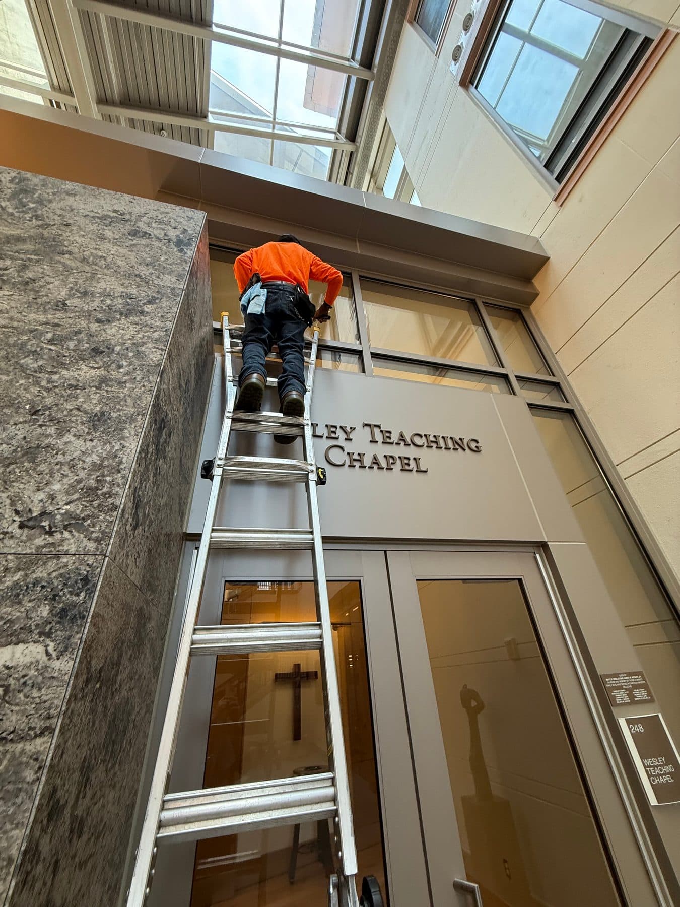 A cleaner on a ladder at the glass entry of Wesley Teaching Chapel