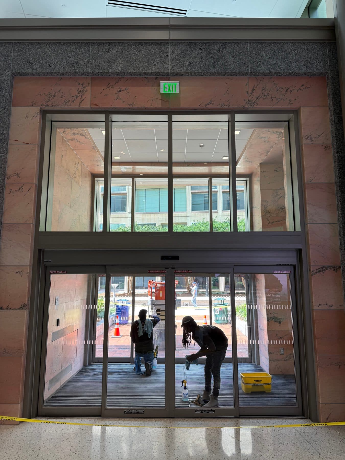 Two cleaners washing a commercial entry door and the transom windows above it