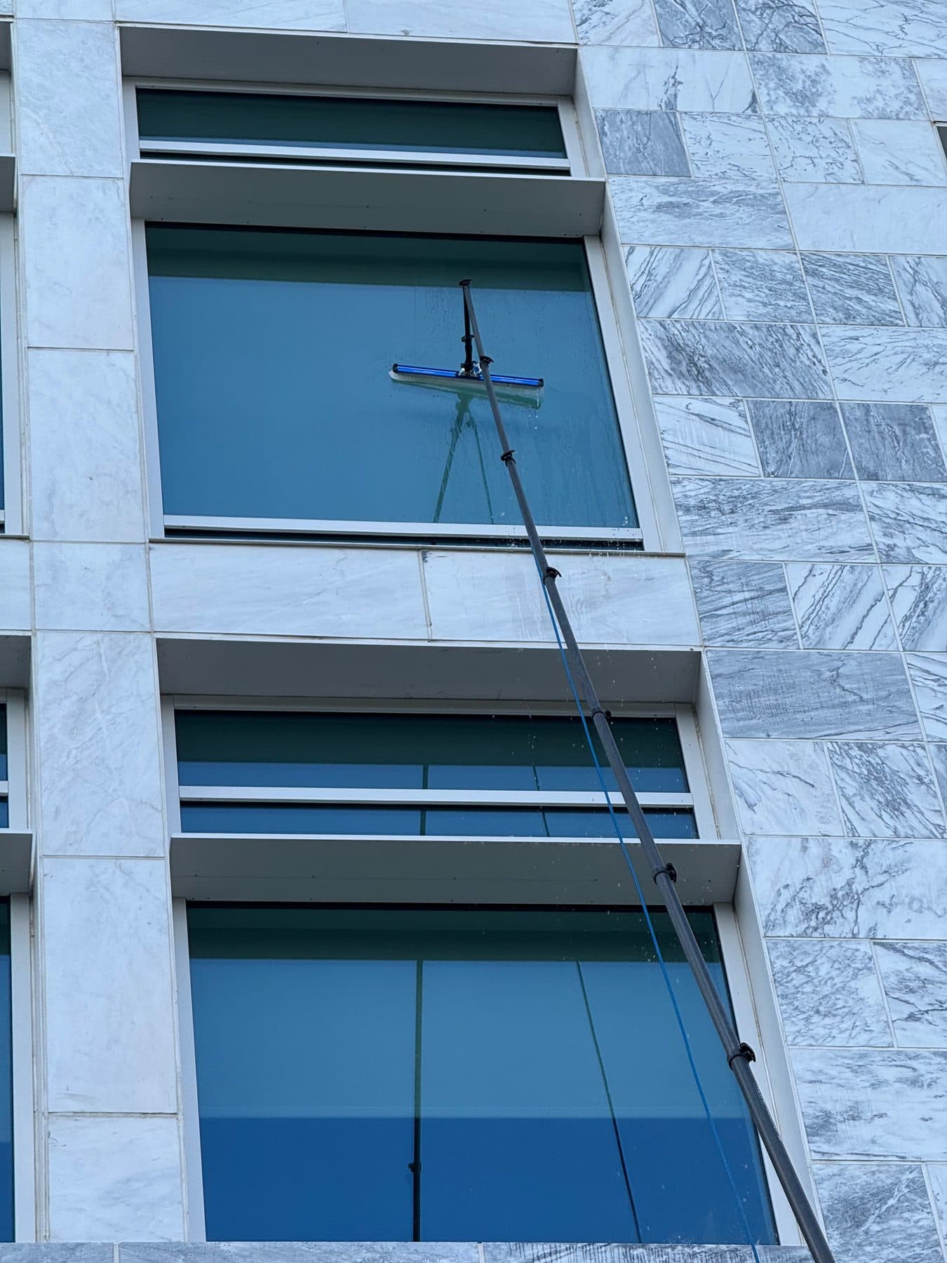 A water-fed pole and squeegee on the windows of a white stone building
