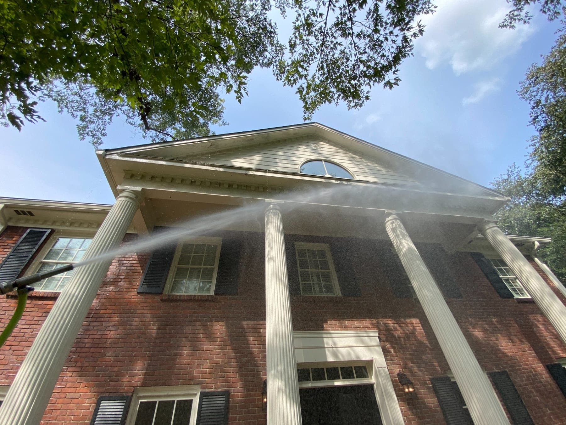 A soft wash spraying across the brick and white columns of a two-story house
